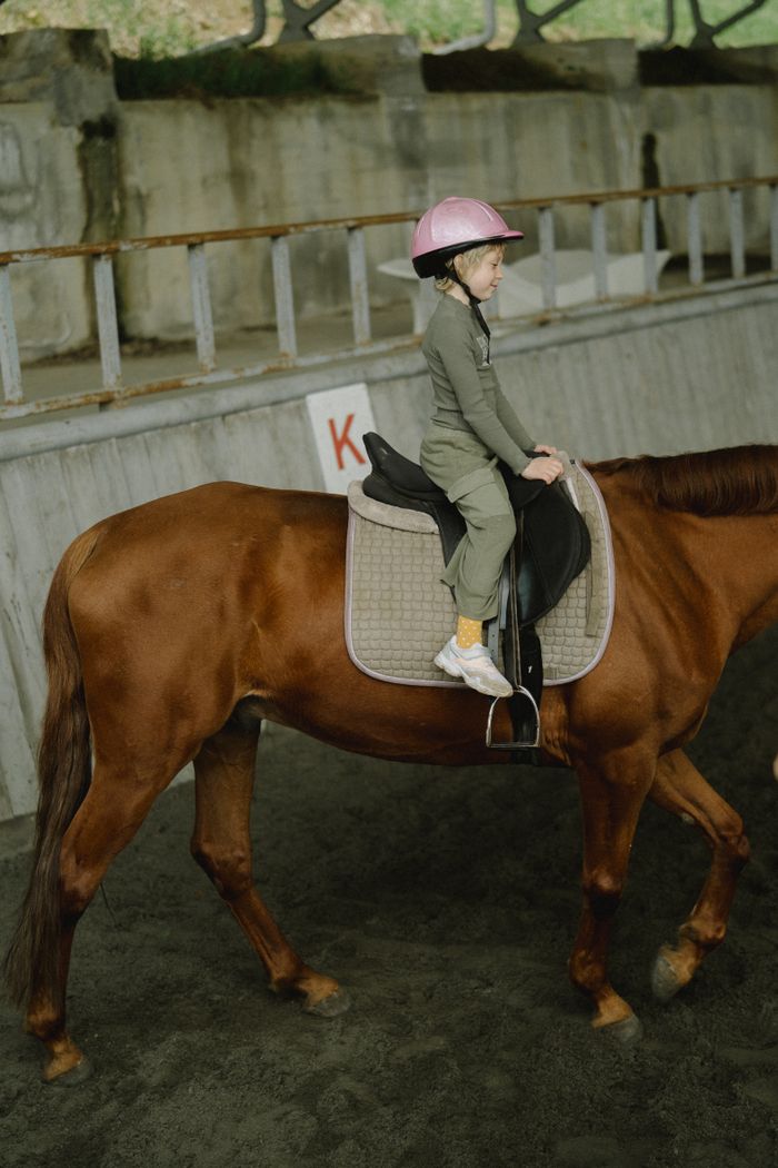 Child enjoying horseback riding indoors, showcasing equestrian experience.