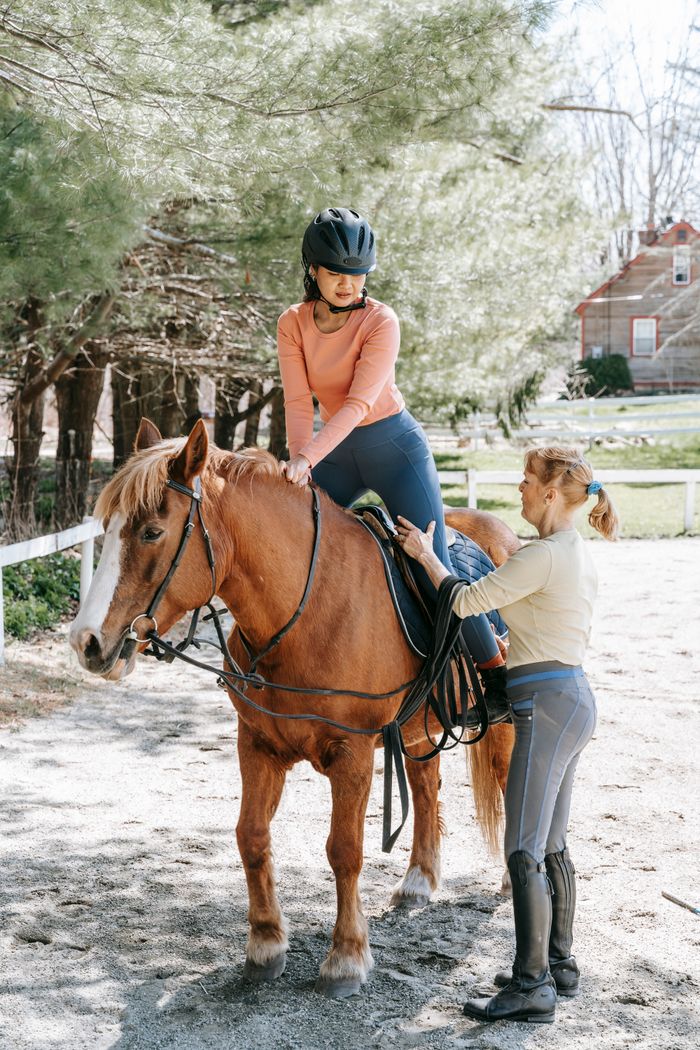 services-02 Two women during a horseback riding lesson in a sunny outdoor setting.